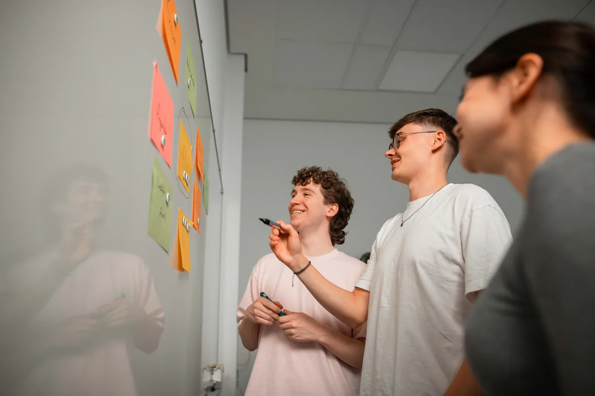 Drei Teammitglieder arbeiten gemeinsam an einem Whiteboard