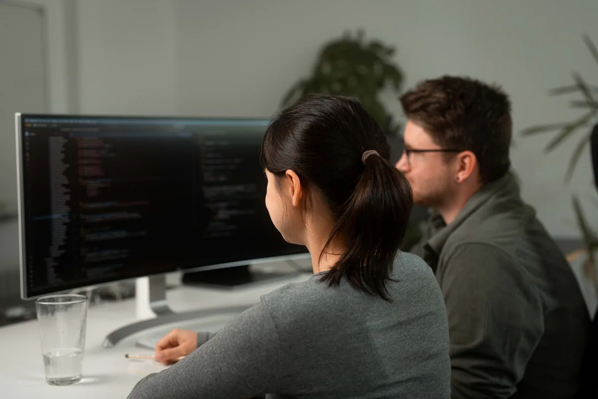 Zwei Teammitglieder besprechen gemeinsam Code an einem Bildschirm