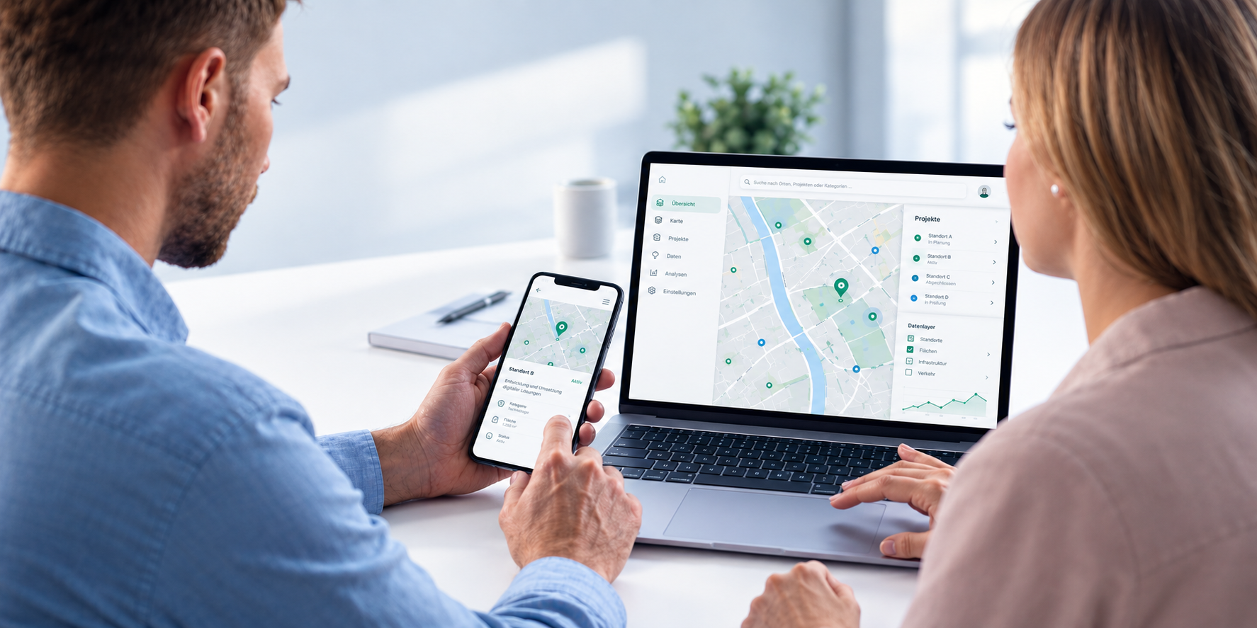 Zwei Personen besprechen eine kartenbasierte Anwendung auf Laptop und Smartphone.